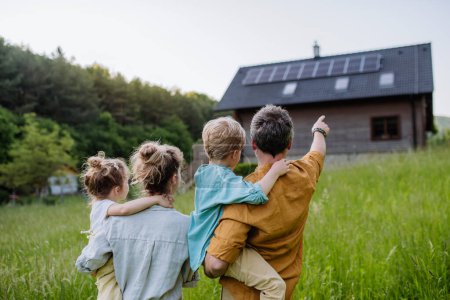Joyeux famille devant leur maison avec des panneaux solaires sur le toit.