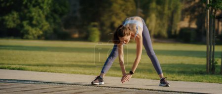 Photo for Full lenght portrait of beautiful fitness woman stretching before outdoor workout in the city park. Healthy lifestyle concept. Banner with copy space. - Royalty Free Image
