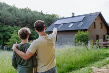 Père montrant un toit avec des panneaux solaires à son fils. Énergie alternative, économies de ressources et concept de mode de vie durable.