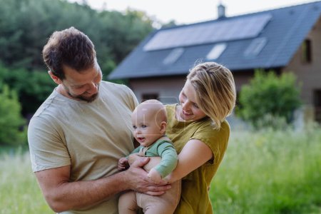 Téléchargez les photos : Famille heureuse près de leur maison avec des panneaux solaires. Énergie alternative, économies de ressources et concept de mode de vie durable. - en image libre de droit
