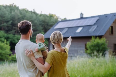 Rückansicht einer Familie in der Nähe ihres Hauses mit Sonnenkollektoren. Alternative Energien, Ressourcenschonung und nachhaltiges Lebensstilkonzept.