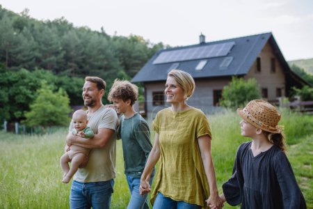 Foto de Familia feliz cerca de su casa con paneles solares. Energía alternativa, ahorro de recursos y concepto de estilo de vida sostenible. - Imagen libre de derechos