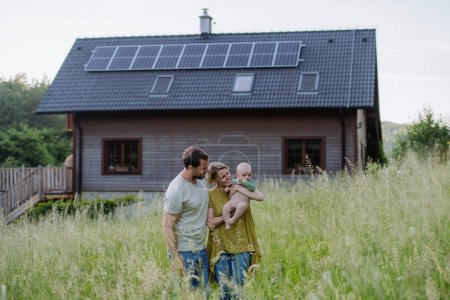 Téléchargez les photos : Famille heureuse avec bébé près de leur maison avec des panneaux solaires. Énergie alternative, économies de ressources et concept de mode de vie durable. - en image libre de droit