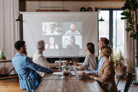 Photo for Employees having online business conference video call on wall display screen in board meeting room. Videoconference presentation, global virtual group corporate online meeting concept. - Royalty Free Image