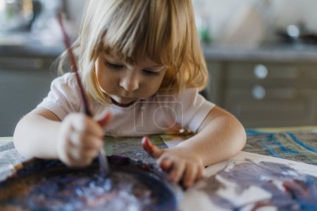 Photo for Cute little girl painting with tempera paint at home, using a paintbrush. - Royalty Free Image
