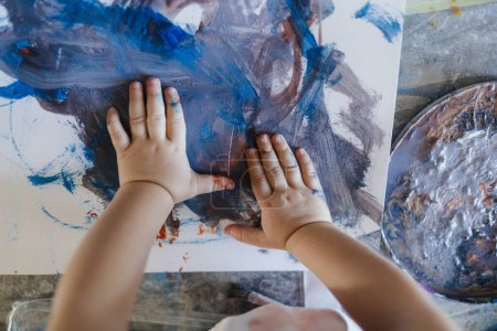 Foto de Linda niña pintando con sus propias manos, usando pintura tempera. Pintura de dedos actividad creativa. - Imagen libre de derechos