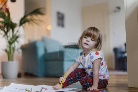 Foto de Linda niña dibujando con lápices de colores, sentada en el suelo en la sala de estar. Delineando su propio pie sobre papel. - Imagen libre de derechos