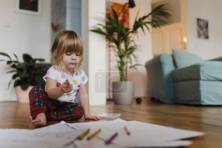 Foto de Linda niña dibujo con lápices de colores, sentado en el suelo en la sala de estar. - Imagen libre de derechos