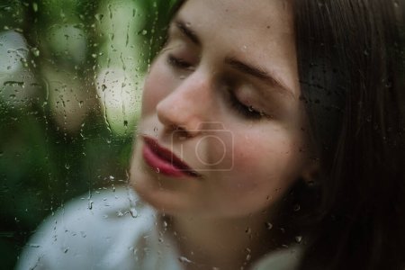 Téléchargez les photos : Portrait d'une jeune femme dans une serre brumeuse à travers un verre brumeux avec des gouttelettes d'eau. - en image libre de droit