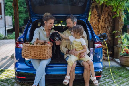 Téléchargez les photos : Joyeux famille assis dans un coffre de voiture et attendant la charge, préparatifs pour le pique-nique. - en image libre de droit