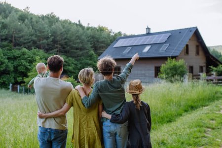 Vue arrière de la famille près de leur maison avec un panneau solaire. Énergie alternative, économies de ressources et concept de mode de vie durable.