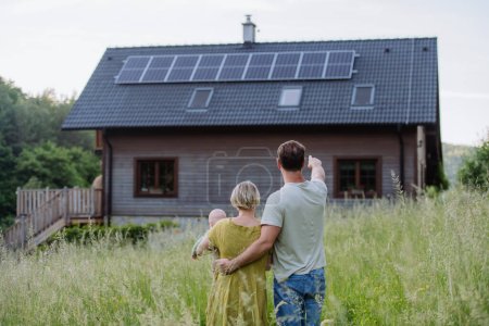 Vue arrière de la famille près de leur maison avec un panneau solaire. Énergie alternative, économies de ressources et concept de mode de vie durable.
