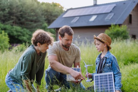 Téléchargez les photos : Père et ses enfants debout devant leur maison avec photovoltaïque sur le toit. - en image libre de droit