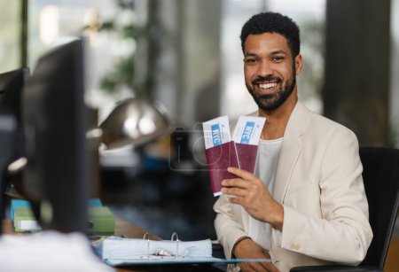 Téléchargez les photos : Jeune homme heureux tenant des billets d'avion dans un bureau. - en image libre de droit