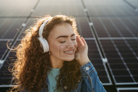 Téléchargez les photos : Portrait de jeune femme excitée, propriétaire sur le toit avec panneaux solaires, écouter de la musique. - en image libre de droit