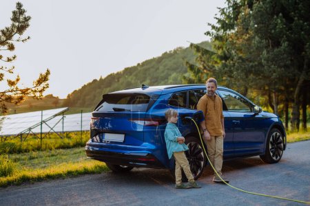 Foto de Padre y su hijo cargando teir coche eléctrico durante el viaje. - Imagen libre de derechos