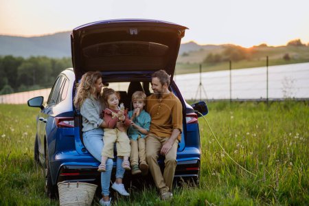 Foto de Familia feliz sentado en un maletero del coche y esperando la carga, preparacionespara el picnic. - Imagen libre de derechos