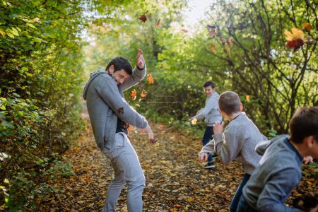 Foto de Padre con sus hijos divirtiéndose en el bosque, arrojando follaje. - Imagen libre de derechos