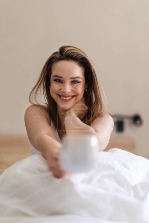 Téléchargez les photos : Femme heureuse assise sur son lit avec une tasse de café. - en image libre de droit