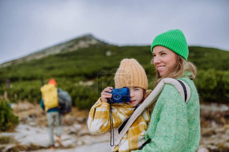Photo for Little girl taking pictures during a hike. Happy family hiking together in an autumn mountains. - Royalty Free Image