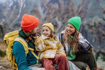 Photo for Happy family resting, having snack and enjoying the view during hiking together in an autumn mountains. Mom, dad and daughter on kid friendly hike. - Royalty Free Image