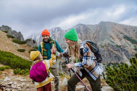 Photo for Portrait of happy family of mother, father and daughter on kid friendly hike in an autumn mountains. Mom and little girl giving high five. - Royalty Free Image
