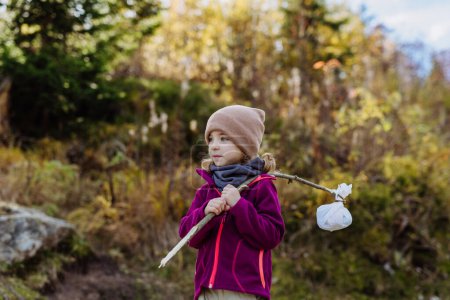 Téléchargez les photos : Portrait de petite fille avec bindle lors d'une randonnée automnale en montagne. Fille tenant bâton avec tissu portant collation à l'intérieur. - en image libre de droit