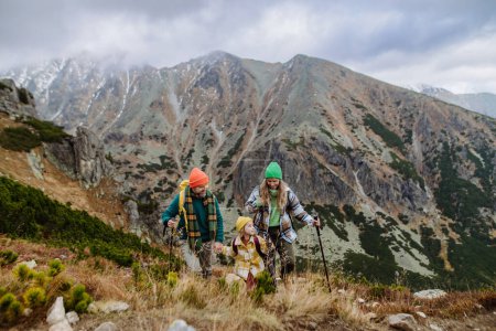 Foto de Retrato de familia feliz de tres con bastones de trekkiing caminando juntos en una montaña de otoño. Senderismo con niños pequeños. - Imagen libre de derechos