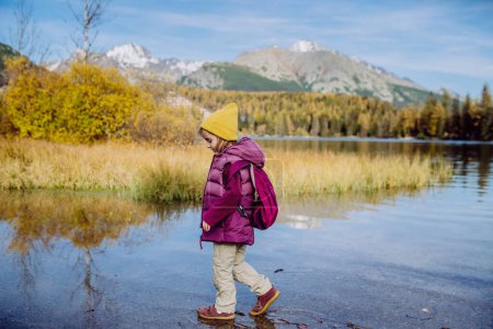 Téléchargez les photos : Petite fille marchant au bord du lac, au milieu d'une belle nature automnale. - en image libre de droit