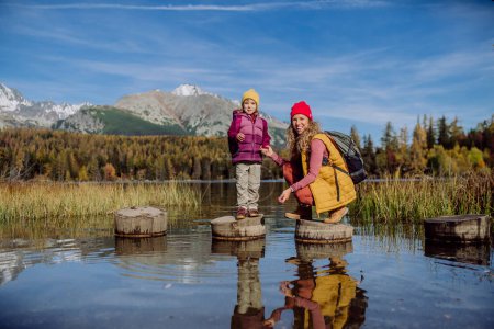 Foto de Madre con hija de pie en escalones de madera en la orilla del lago en las montañas. Turista femenina con niño pequeño disfrutando de vistas a las montañas. - Imagen libre de derechos