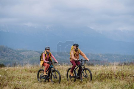 Foto de Yung feliz pareja en las bicicletas, en medio de la naturaleza de otoño. Pareja casada pasando sus lunas de miel senderismo, mochilero, visitando parques nacionales. - Imagen libre de derechos