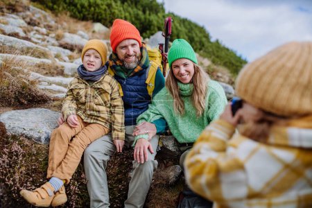 Photo for Little girl taking pictures of her family during a hike. Happy family hiking together in an autumn mountains. - Royalty Free Image