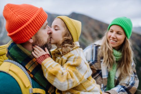 Photo for Portrait of happy family of mother, father and daughter on kid friendly hike in an autumn mountains. Little girl giving kiss to her father. - Royalty Free Image