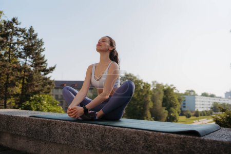 Foto de Vista frontal de una joven deportista haciendo ejercicios de respiración en la colchoneta del gimnasio después del entrenamiento en la ciudad. Mujer meditar al aire libre, en el parque. - Imagen libre de derechos