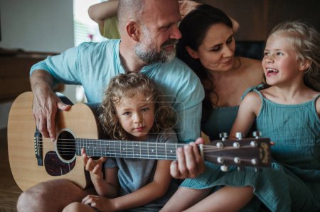 Téléchargez les photos : Père jouant à la guitare pour sa famille. Famille s'amuser et chanter ensemble. Concept de lien familial. - en image libre de droit