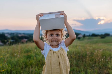 Téléchargez les photos : Petite fille avec maison modèle avec installation de panneaux solaires, debout au milieu de la prairie. Concept d'énergie alternative, d'économies de ressources et de mode de vie durable. . Importance de - en image libre de droit