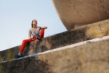 Photo for Young fitness woman in sportswear resting after hard workout session in the city. Sporty woman catching breath and drinking water after morning excercise. - Royalty Free Image