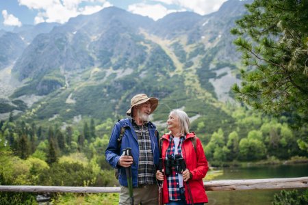 Photo for Active elderly couple hiking together in autumn mountains, on senior friendly trail. Senior spouses on the vacation in the mountains celebrating anniversary. Senior tourists with backpacks using - Royalty Free Image