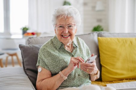 Téléchargez les photos : Patients âgés diabétiques utilisant un glucomètre continu pour vérifier leur glycémie à la maison. Dispositif de MGM facilitant la vie des femmes âgées, aidant à gérer sa maladie et se concentrant sur d'autres activités - en image libre de droit