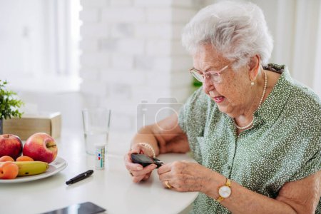 Diabetische Seniorin überprüft ihren Blutzuckerspiegel mit einem Fingerstick-Messgerät. Porträt einer Seniorin mit Typ-1-Diabetes mit Blutzuckermessgerät zu Hause.