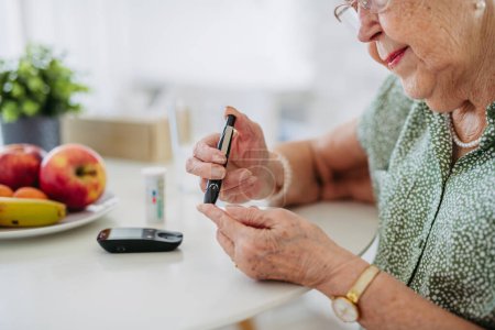 Diabetic senior patient checking her blood sugar level with fingerstick testing glucose meter. Portrait of senior woman with type 1 diabetes using blood glucose monitor at home.