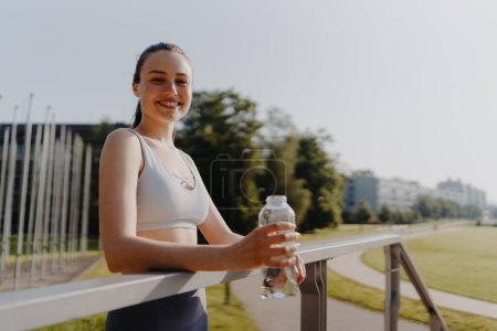 Foto de Retrato de mujer deportista bebiendo agua de la botella después de la sesión de entrenamiento. Importancia de la hidratación durante el entrenamiento. - Imagen libre de derechos
