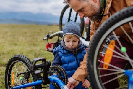 Photo for Littlle boy helping father attache a bicycle on bike carrier. Preparing for bicycle ride in nature, putting off bicycles from car racks. Concept of healthy lifestyle and moving activity. - Royalty Free Image