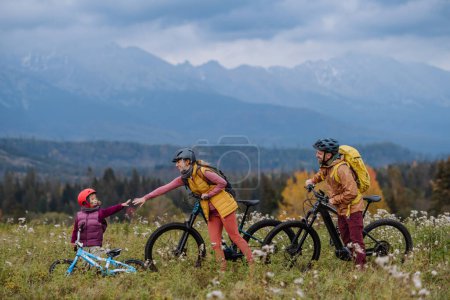Photo for Side view of young family with little daughter at bicycles, in the middle of autumn nature.Concept of healthy lifestyle. Mom and daughter holding hands. - Royalty Free Image