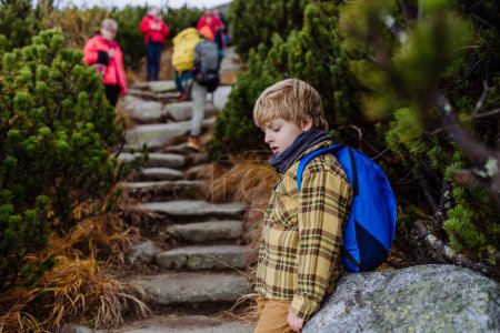 Photo for Portrait of tired young boy resting during hard hike in a autumn mountains. Hiking with young kids on difficult terrain. - Royalty Free Image