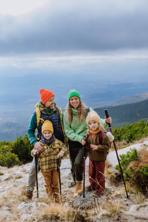 Téléchargez les photos : Portrait de famille heureuse avec bâtons de trekki randonnée ensemble dans une montagne d'automne. Randonnée avec les jeunes enfants. - en image libre de droit