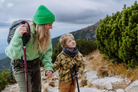 Foto de Madre activa e hijo pequeño con bastones de trekkiing caminando juntos en una montaña de otoño. Senderismo con niños pequeños. - Imagen libre de derechos