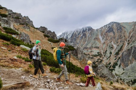 Photo for Portrait of happy family with trekkiing poles hiking together in an autumn mountains. Hiking with young kids. Family hikers walking down the hill. - Royalty Free Image