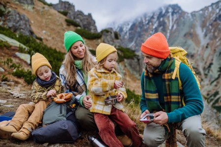 Téléchargez les photos : Joyeux repos en famille, goûter pendant la randonnée ensemble dans une montagne d'automne. - en image libre de droit