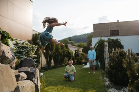 Foto de Padre con dos hijos divirtiéndose juntos en el jardín. Niña saltando desde los escalones de piedra. - Imagen libre de derechos